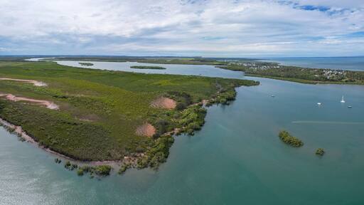 Aerial view of the serpentine river snaking through verdant mangroves, meeting the cerulean sea under a cloudy sky, River Heads, Queensland, Australia.