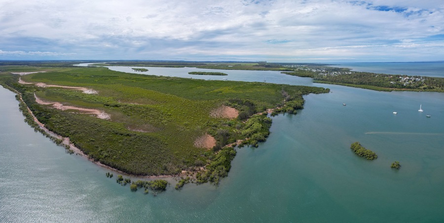Aerial view of the serpentine river snaking through verdant mangroves, meeting the cerulean sea under a cloudy sky, River Heads, Queensland, Australia.