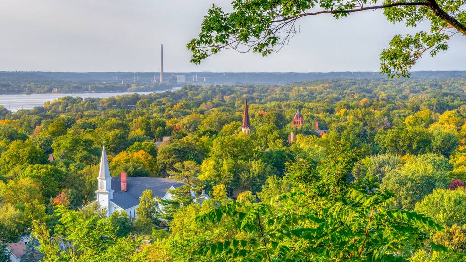 A lush green landscape with a church and a tall chimney in the distance.
