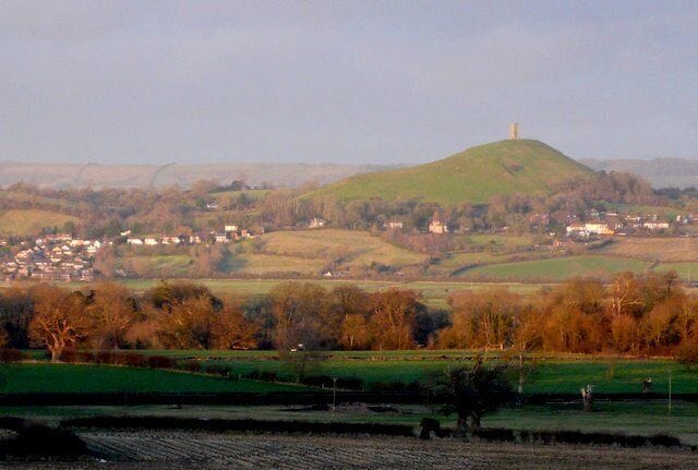 A hill with a tower, a village in the valley, and a field in the foreground.