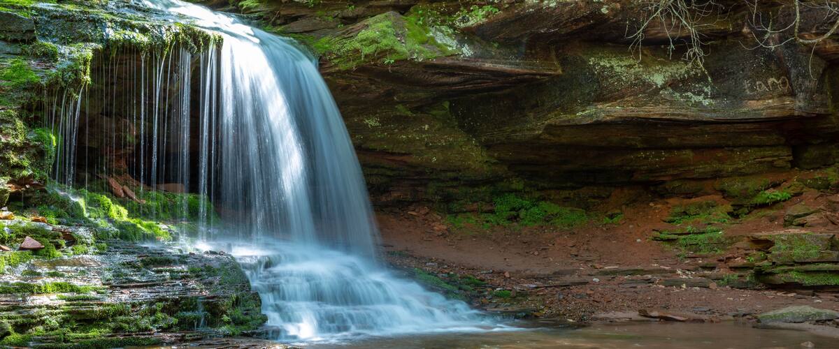 A waterfall cascading over moss-covered rocks into a shallow pool.