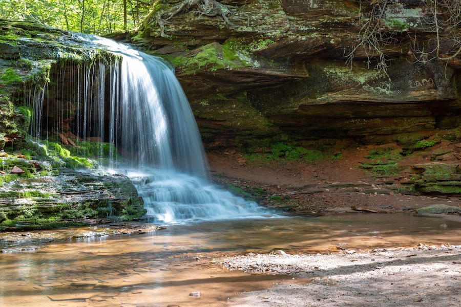 A waterfall cascading over moss-covered rocks into a shallow pool.