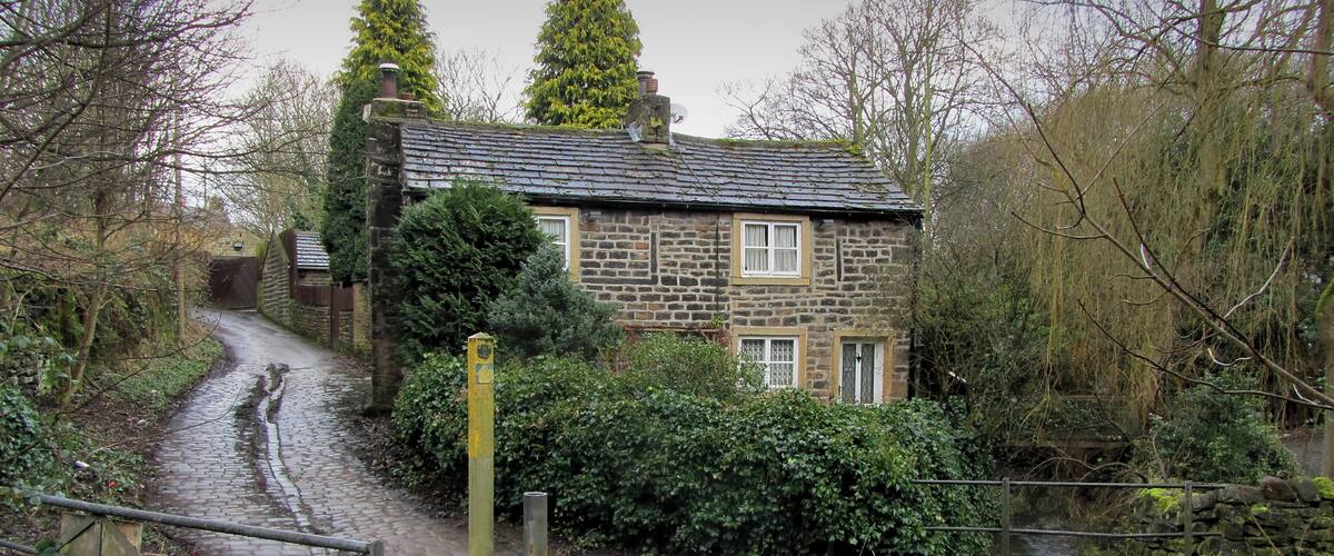 A stone house with a thatched roof by a narrow waterway.