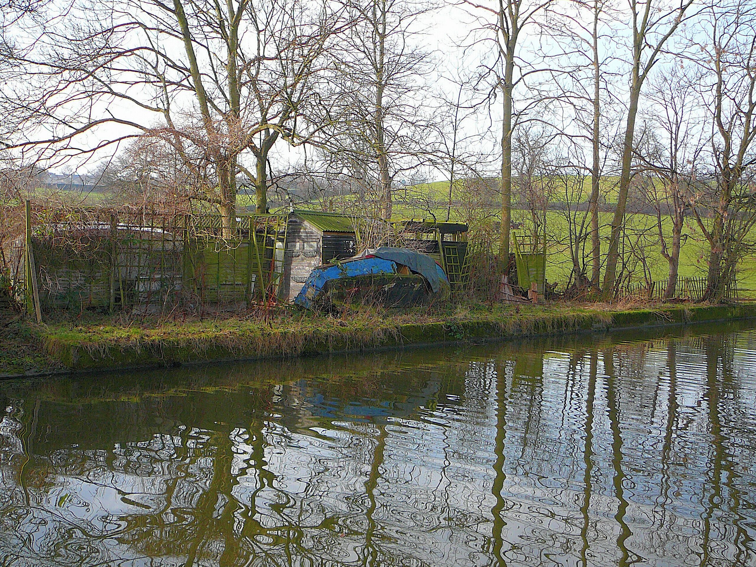 A river with a blue structure partially submerged, surrounded by trees and a fence.