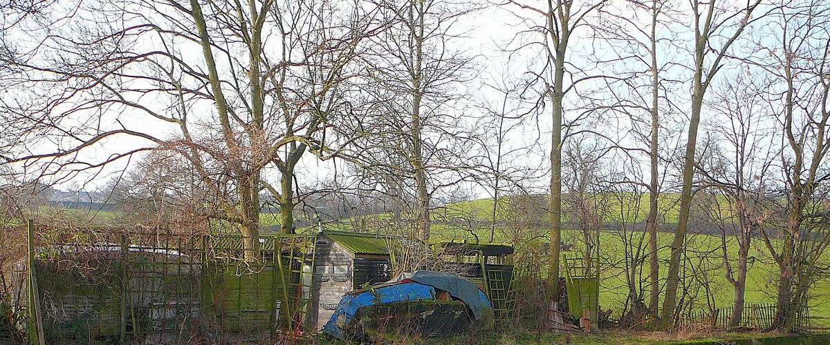A river with a blue structure partially submerged, surrounded by trees and a fence.