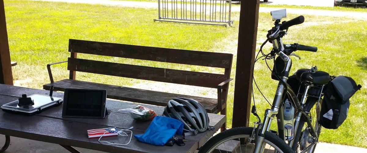 A picnic table with a bicycle, helmet, and a laptop.