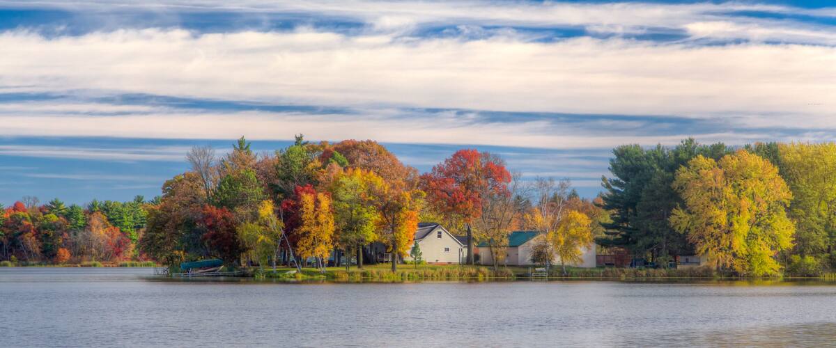 A lake with autumn-colored trees and a house by the water.