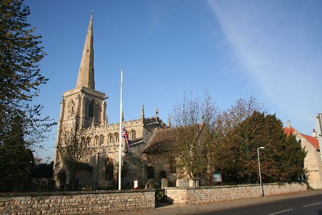A historic church with a tall spire, a stone wall, and a clear blue sky.