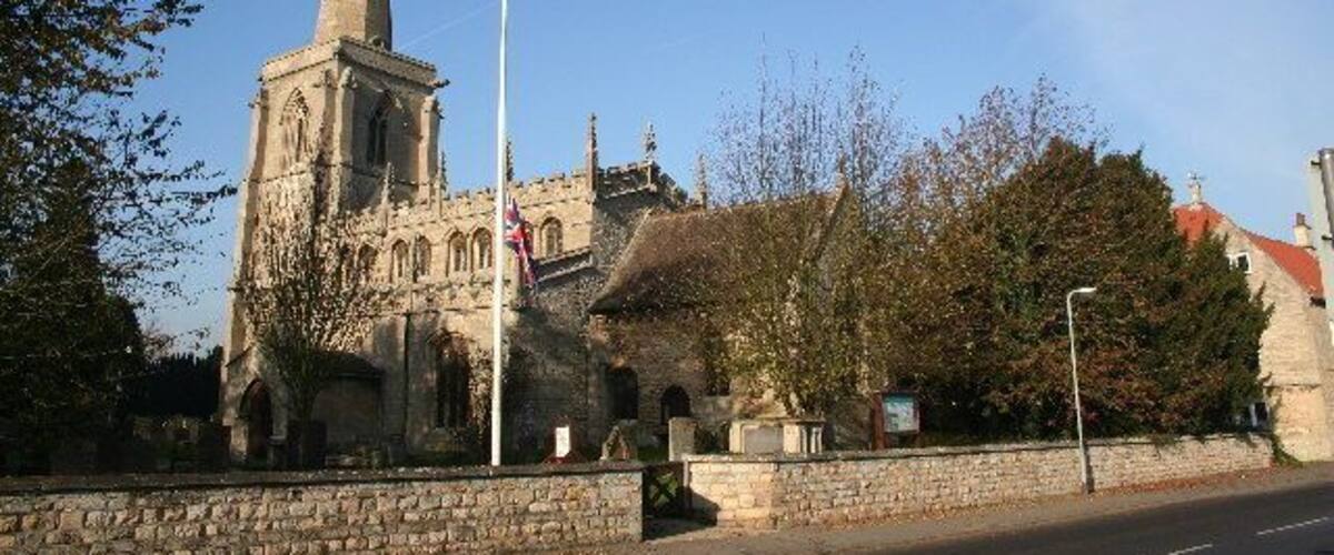 A historic church with a tall spire, a stone wall, and a clear blue sky.