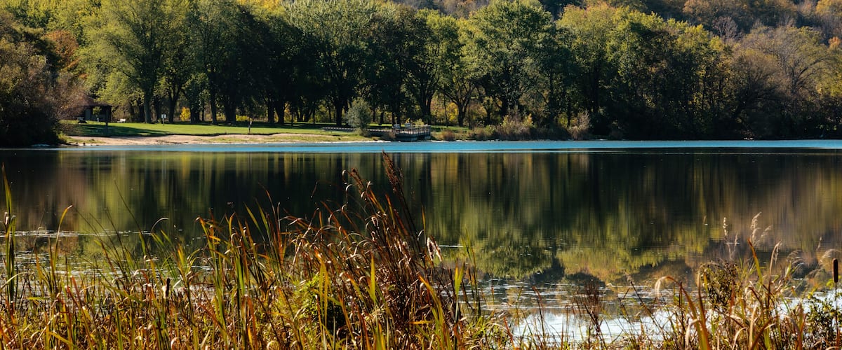 A calm lake surrounded by autumn-colored trees and a small gazebo.