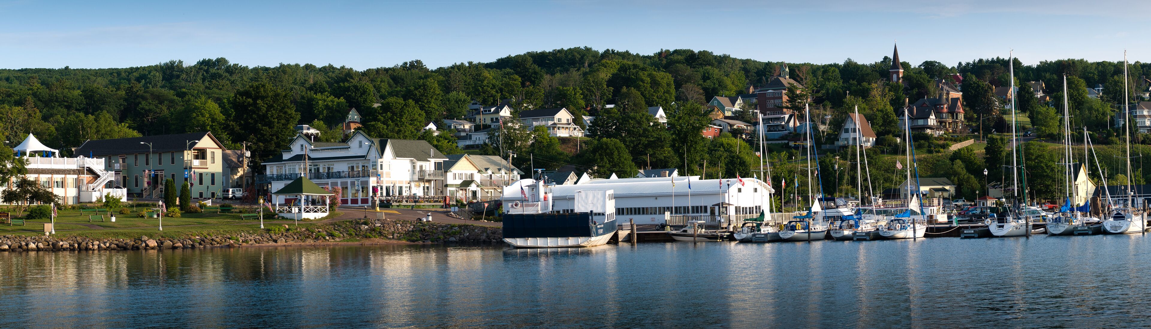 A harbor with boats, a lighthouse, and houses on a hillside.