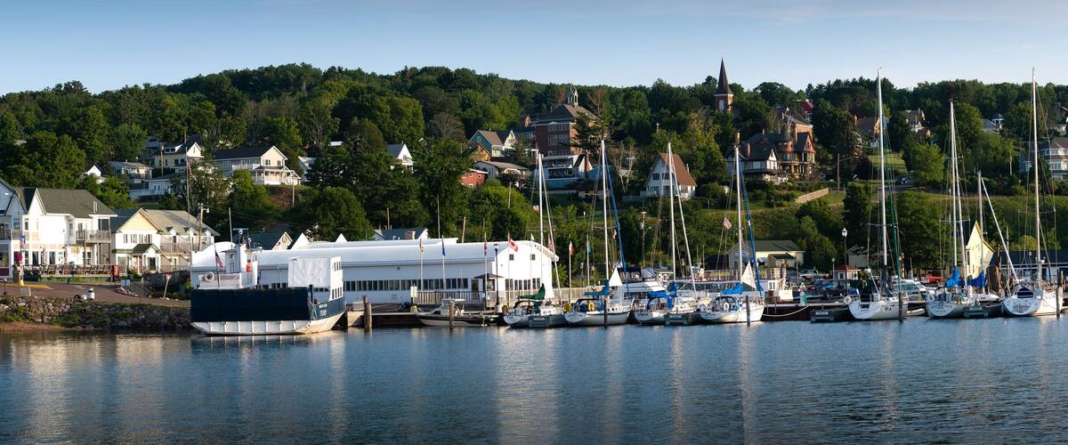 A harbor with boats, a lighthouse, and houses on a hillside.