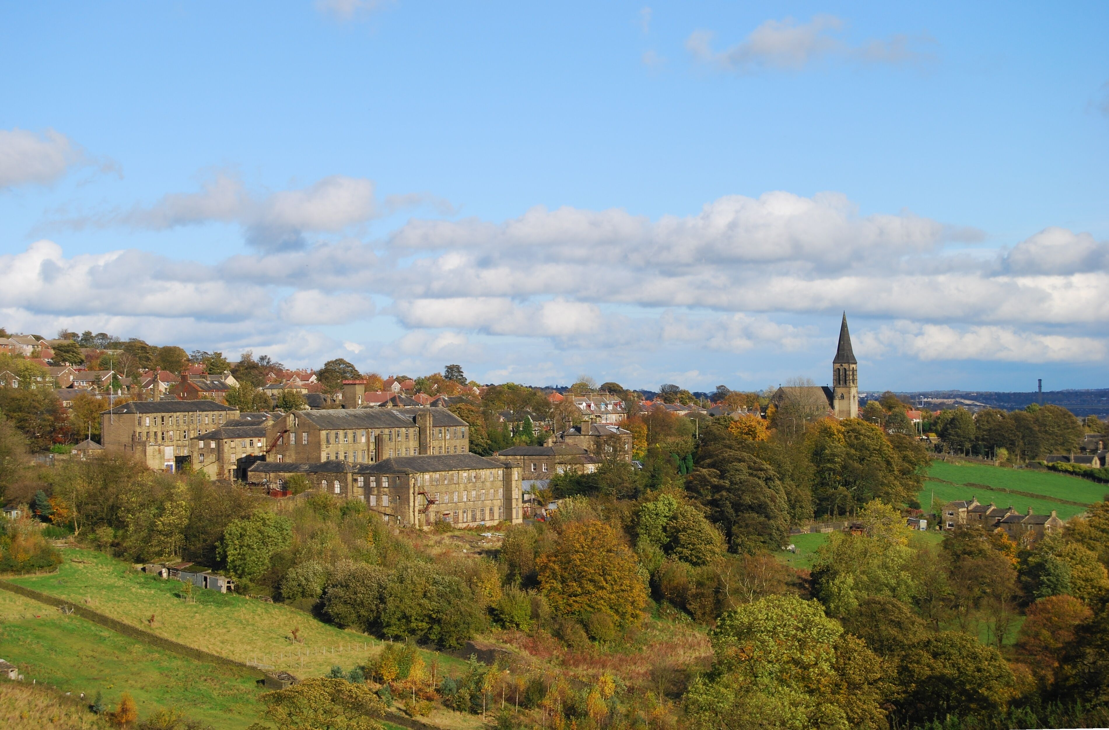 A town with historic buildings, a prominent church tower, and rolling green hills.