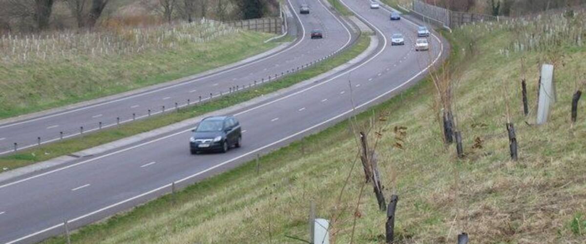 A multi-lane highway curving through a rural landscape with grassy fields and sparse trees.