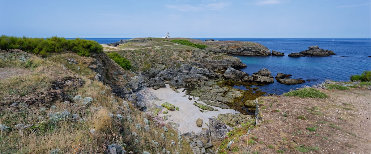 A coastal landscape with rocky terrain, a lighthouse, and the ocean.
