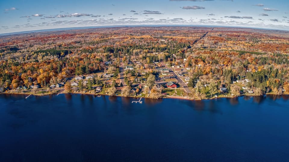 An aerial view of a lakeside community with autumn foliage, a dock, and a clear sky.