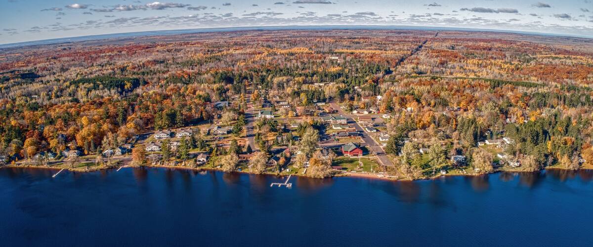 An aerial view of a lakeside community with autumn foliage, a dock, and a clear sky.