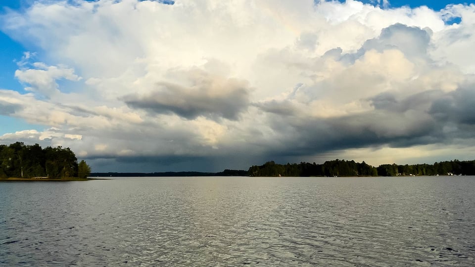 A calm lake with a forested shoreline and a cloudy sky.
