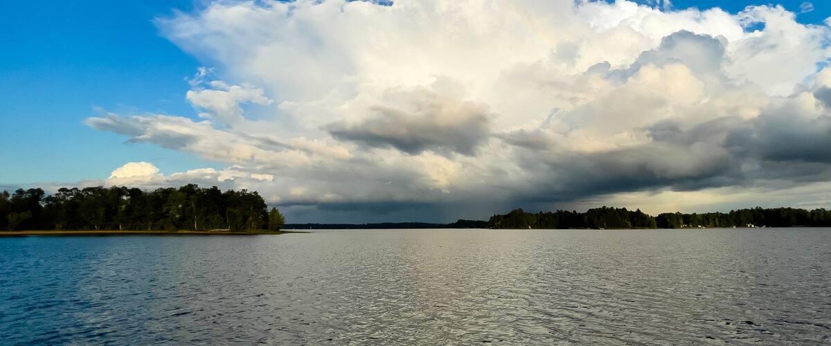 A calm lake with a forested shoreline and a cloudy sky.