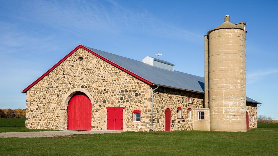 A stone barn with red doors and a silo.