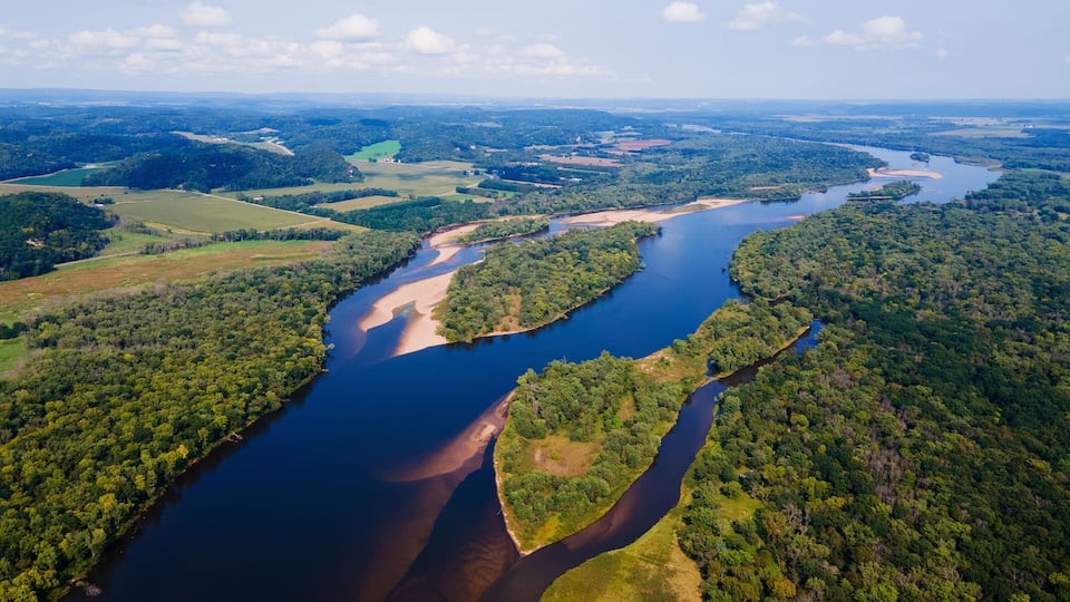 A river winding through a densely forested landscape with clearings and fields.