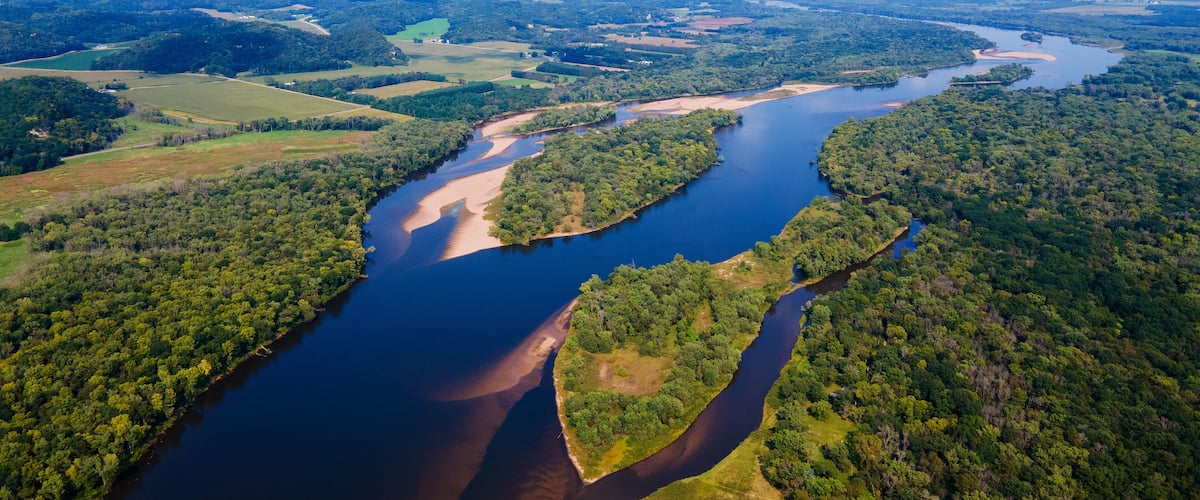 A river winding through a densely forested landscape with clearings and fields.