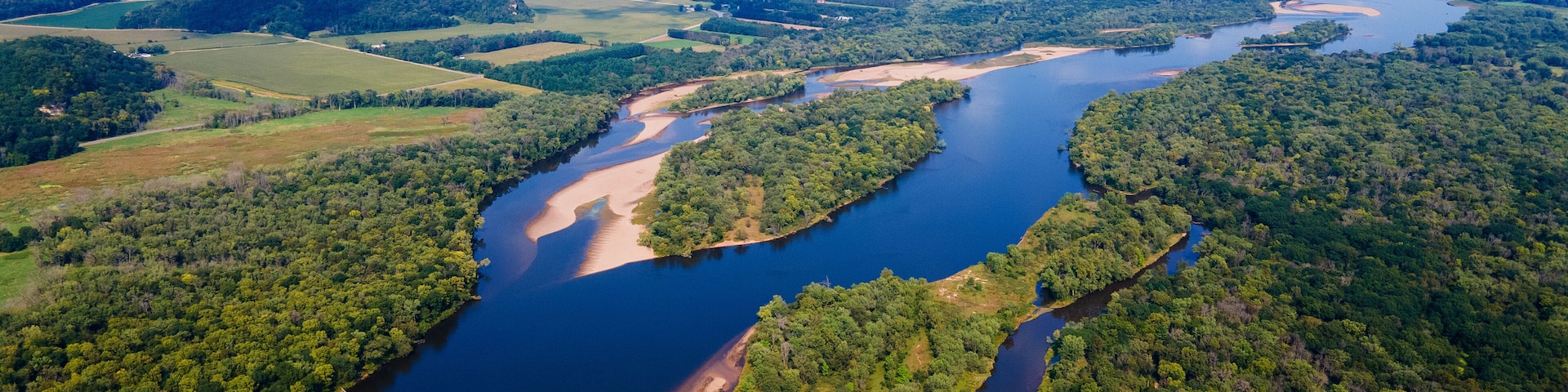 A river winding through a densely forested landscape with clearings and fields.