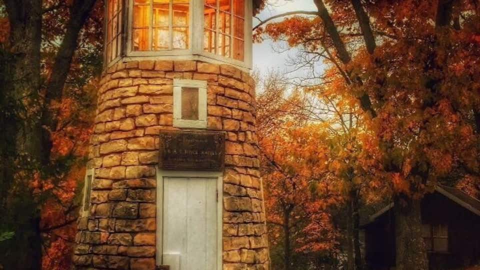 A stone lighthouse with a white door, surrounded by autumn foliage.