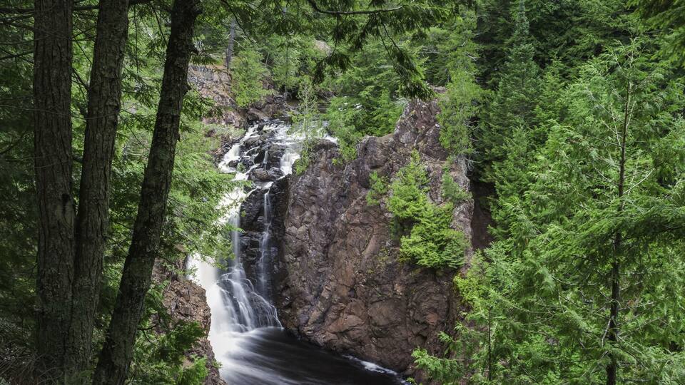 A waterfall cascading down a rocky cliff surrounded by dense green forest.