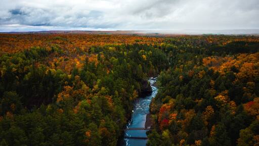 Beautiful aerial above the Bad River and a pedestrian foot bridge at Copper Falls with colorful fall foliage lining the river banks and cloudy sky above the horizon in autumn in Mellen, Wisconsin.