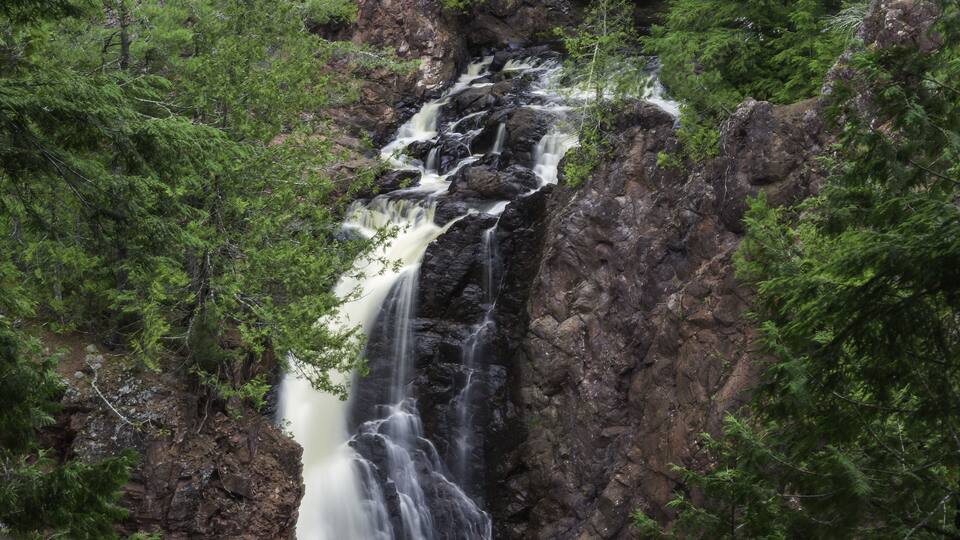 A waterfall cascading down a rocky cliff surrounded by dense green forest.