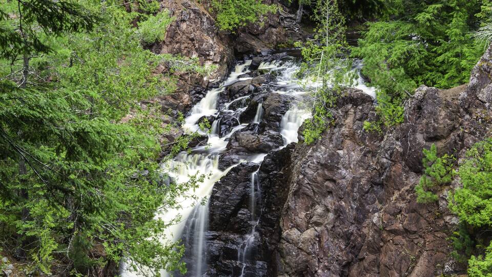 A waterfall cascading over rocky terrain surrounded by dense green foliage.