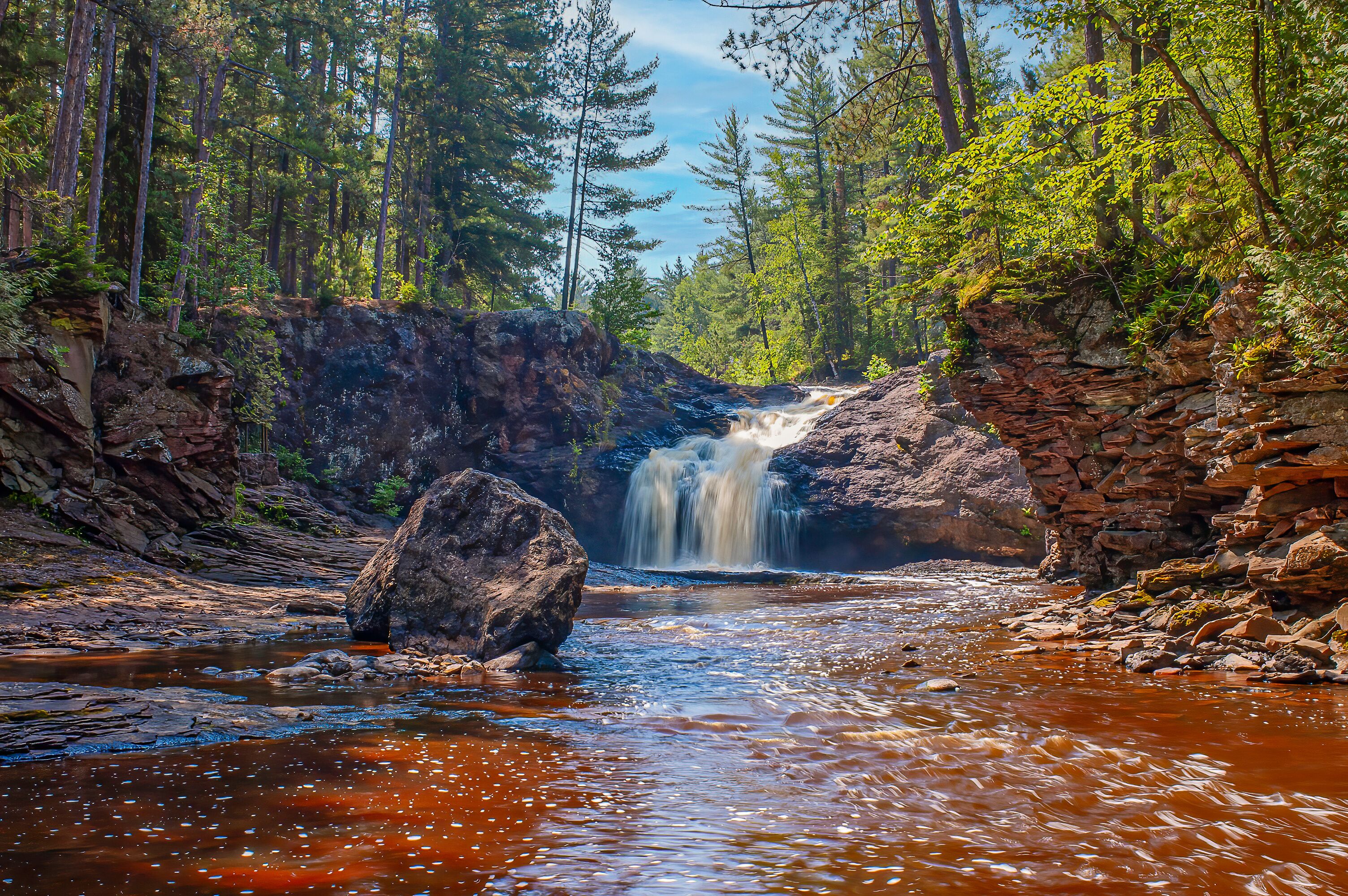 A waterfall cascading over a rocky ledge surrounded by dense forest.