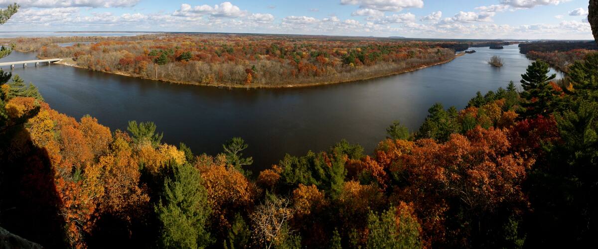 A river surrounded by autumn-colored trees and a bridge in the distance.