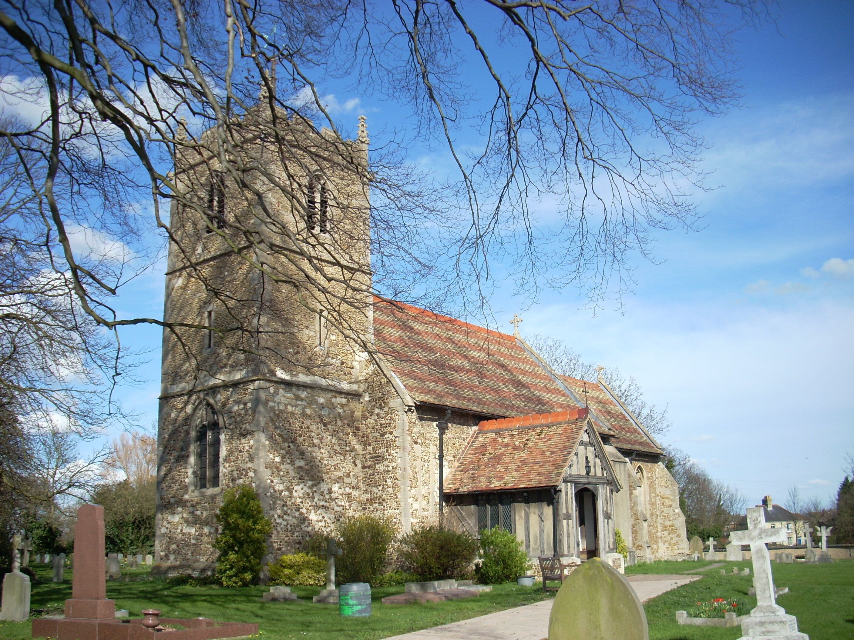 A historic church with a tall tower and a red-tiled roof, surrounded by a cemetery with headstones.