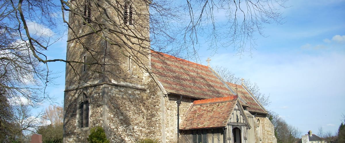 A historic church with a tall tower and a red-tiled roof, surrounded by a cemetery with headstones.