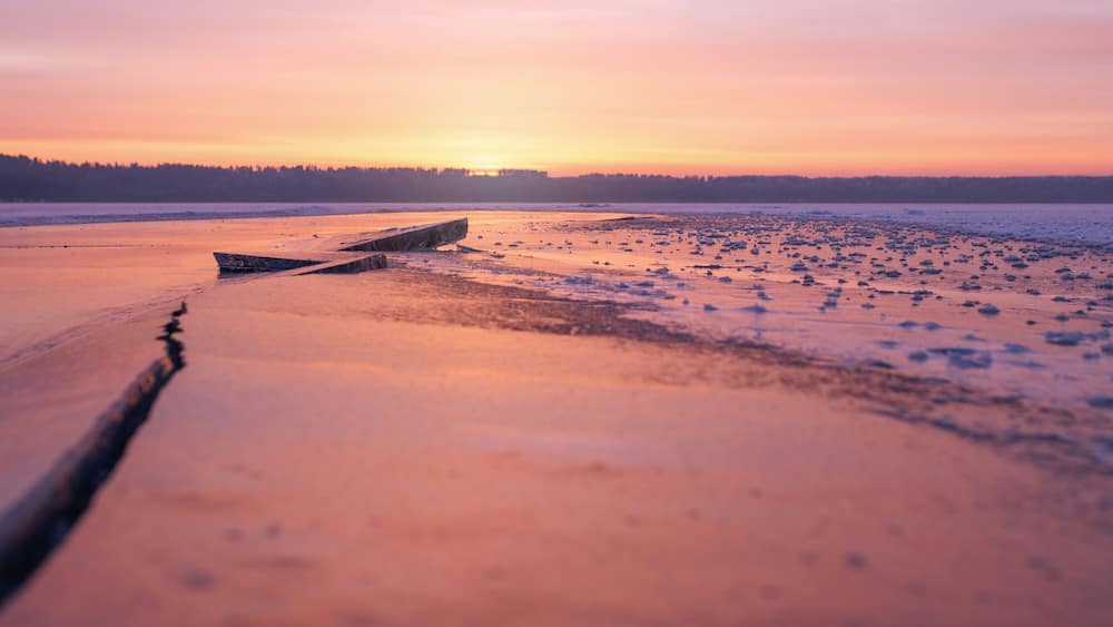 Winter landscape of frozen lake at sunset in warm purple tones.