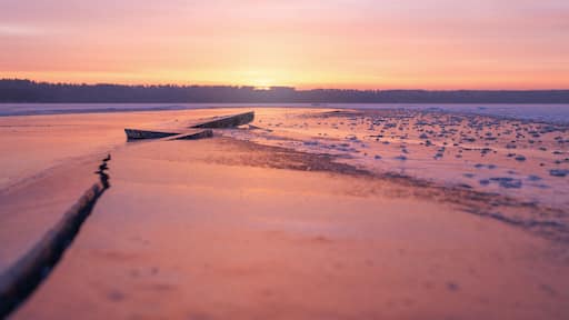 Winter landscape of frozen lake at sunset in warm purple tones.