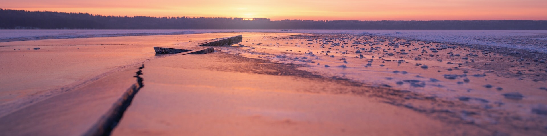 Winter landscape of frozen lake at sunset in warm purple tones.