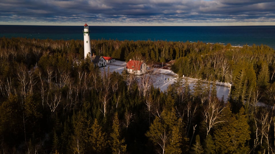 A lighthouse surrounded by dense forest and a small settlement with a red-roofed building.