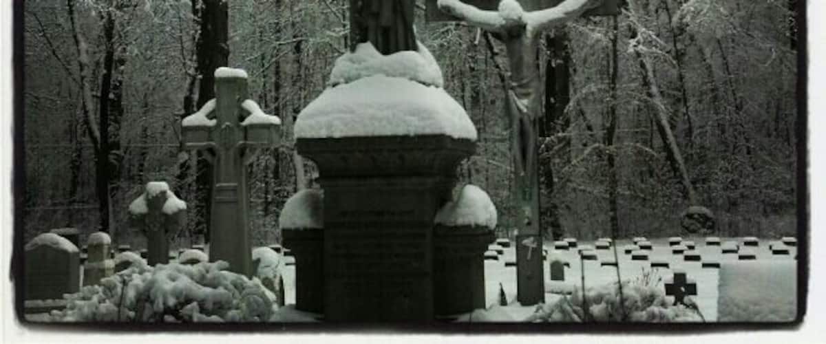 A cemetery with snow-covered gravestones and a crucifixion statue.
