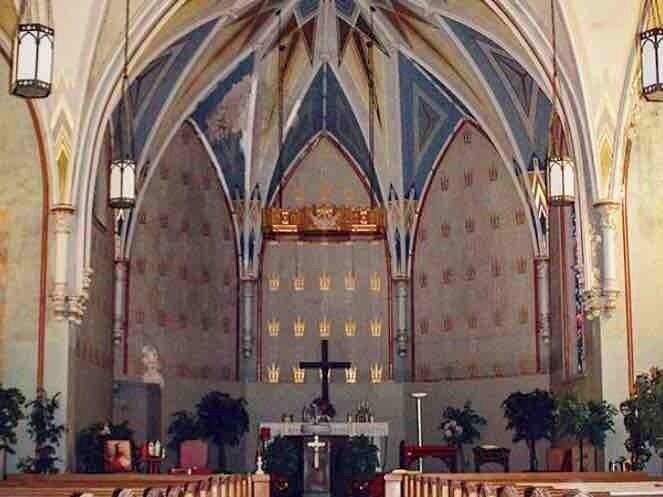 A church interior with Gothic arches, a central altar, and religious statues.