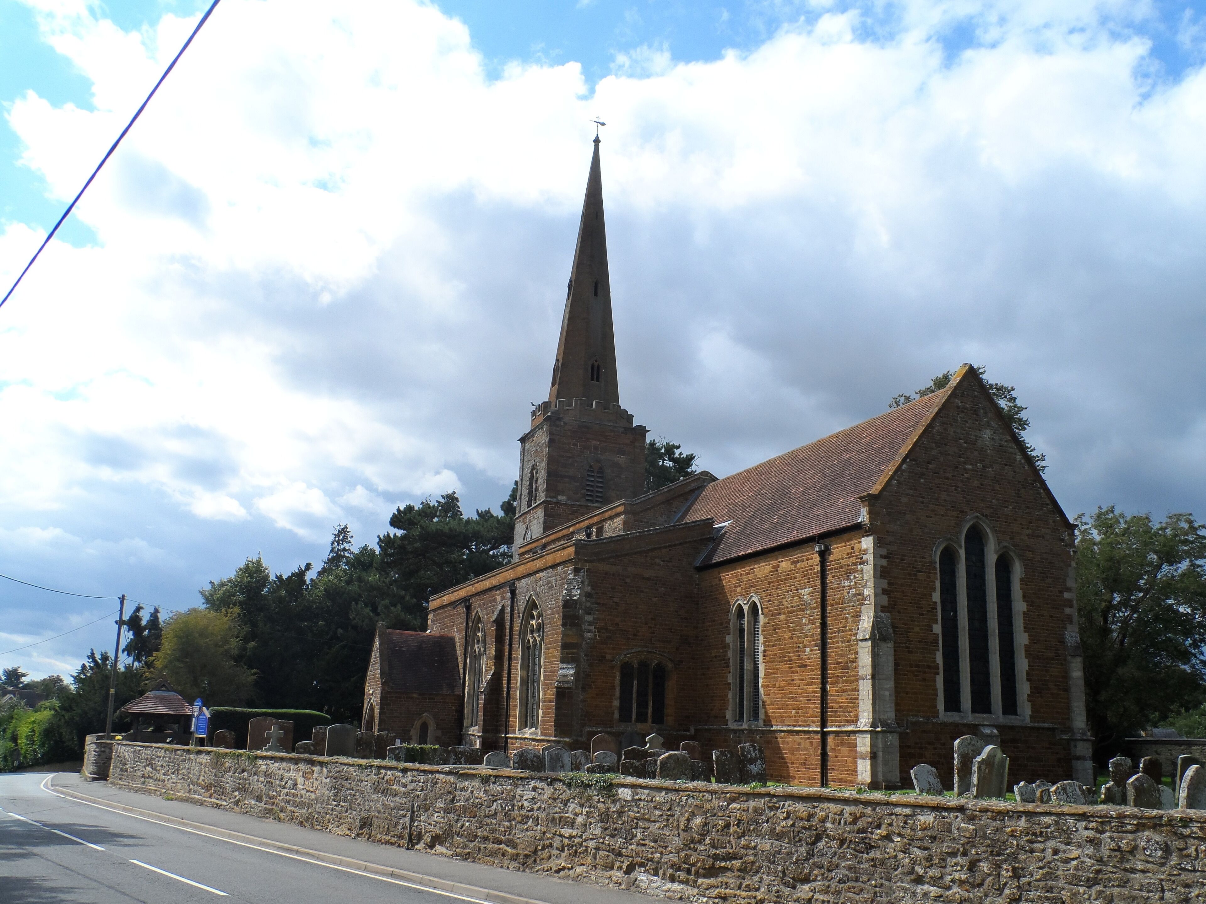 A church with a tall spire and a stone wall with gravestones.