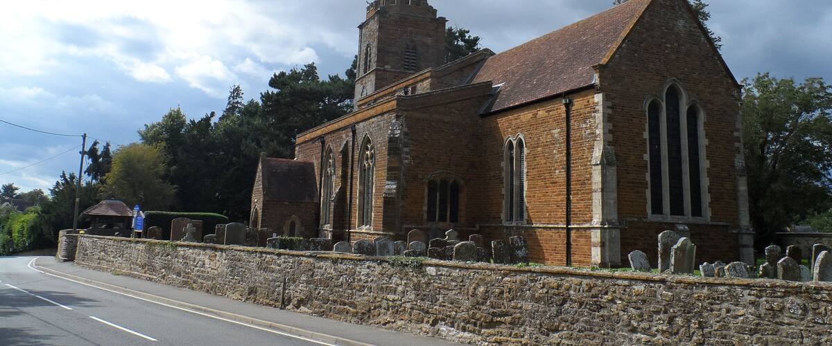 A church with a tall spire and a stone wall with gravestones.