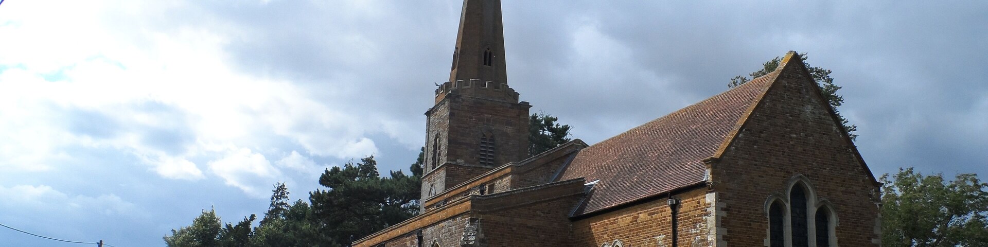A church with a tall spire and a stone wall with gravestones.