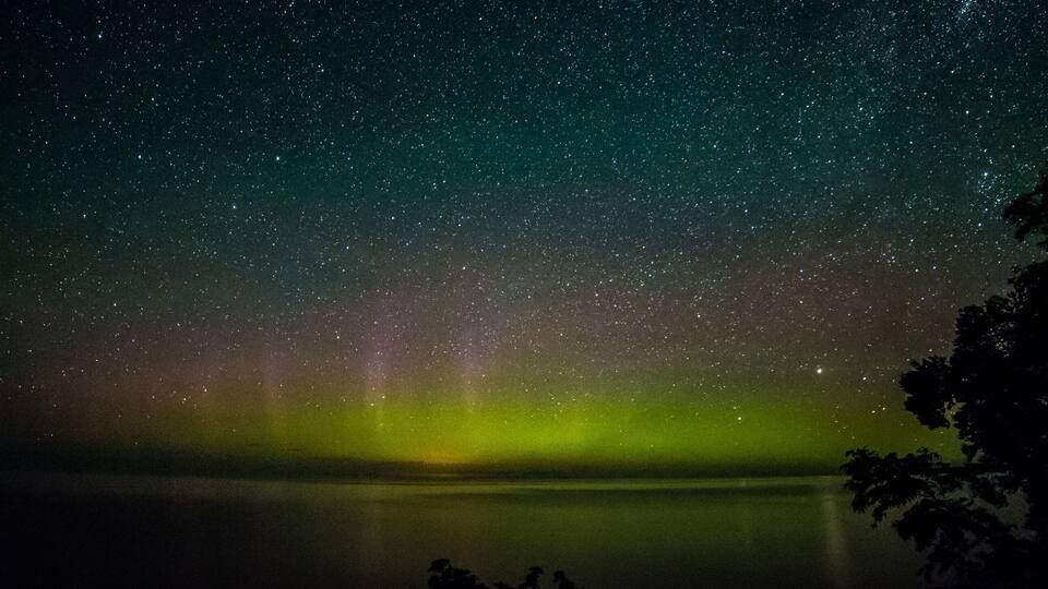 A night sky with stars and the aurora borealis over a calm lake.