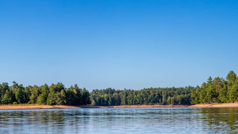 A calm river with sandy banks and dense forest on both sides.