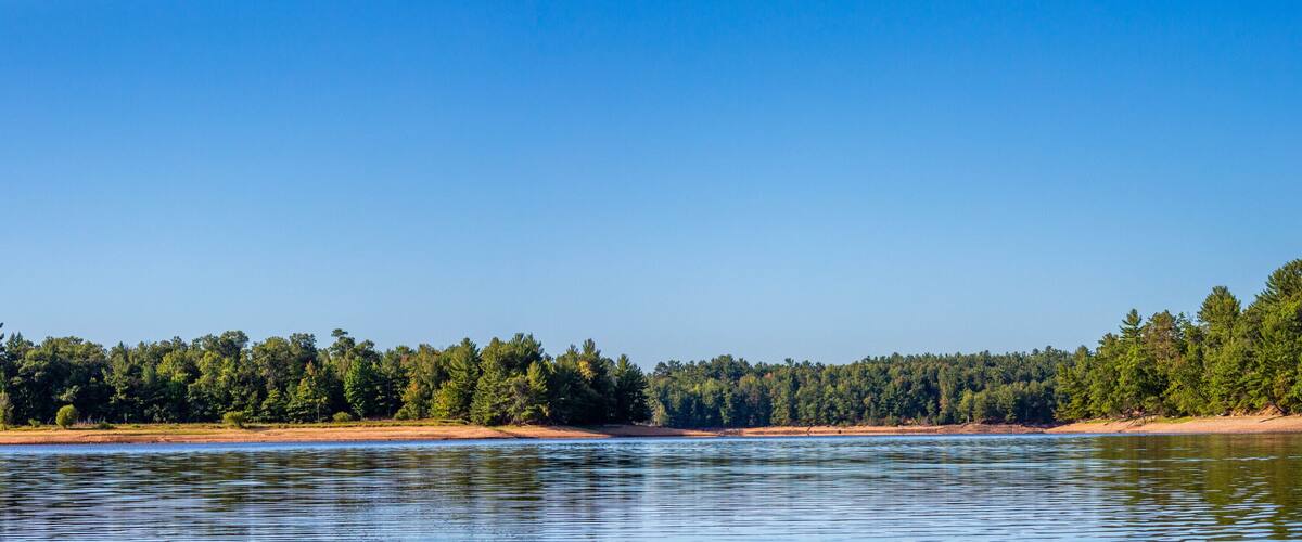 A calm river with sandy banks and dense forest on both sides.