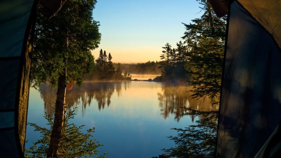 A tent overlooking a calm lake surrounded by trees.