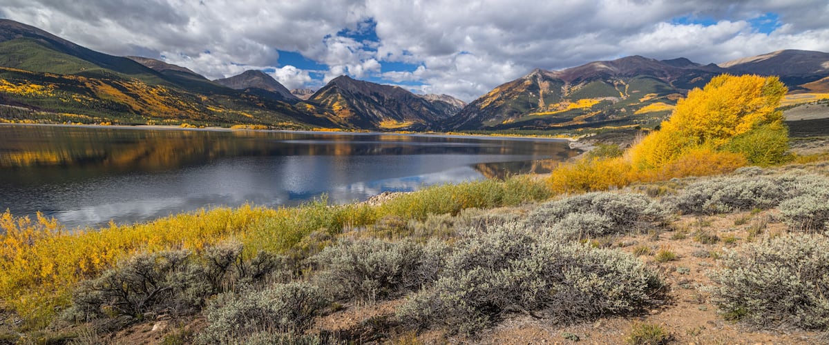 A mountain lake with autumn foliage and rugged terrain.